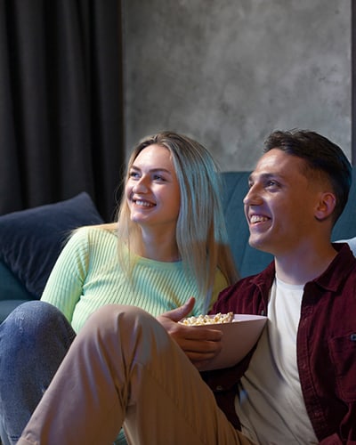 Eine junge Frau und ein junger Mann schauen gemeinsam einen Film mit einem Eimer Popcorn in der Hand
